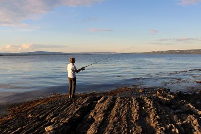 Full length of man fishing on beach against sky