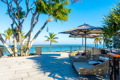 Lounge chairs by swimming pool at beach against blue sky