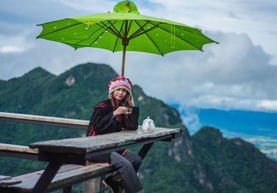 Smiling woman sitting on mountain against sky