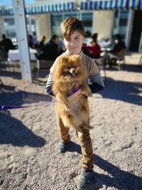 Portrait of boy carrying dog on footpath in city