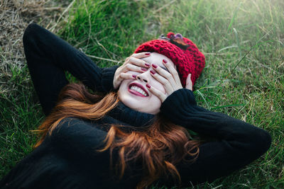 Young woman with face covered by hands lying down on grass
