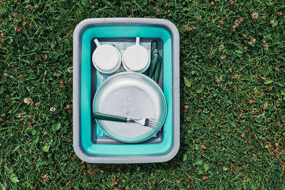 Washing up bowl filled with the washed outdoor dishes, plates, cups and cutlery put on grass on camp