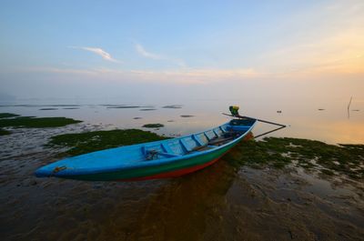 Boat moored on beach against sky during sunset