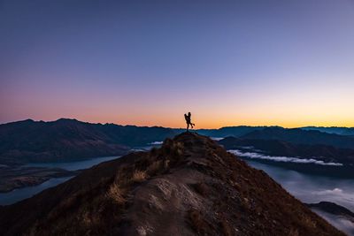 Silhouette man standing on rock against sky during sunset