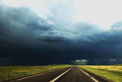 Road passing through landscape against storm clouds