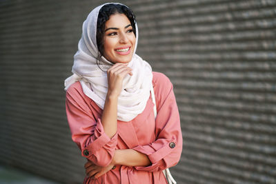 Portrait of smiling young woman standing against wall