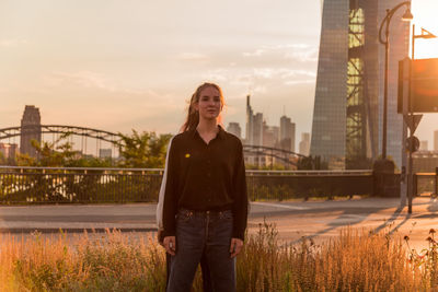 Female friends standing against bridge in city during sunset