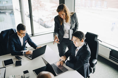 Businesswoman discussing with coworker over laptop while professional working at conference table in corporate office