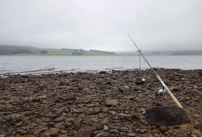 Fishing rod on field by river against sky