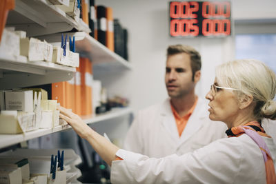 Mature medical colleagues arranging medicines on rack at pharmacy store