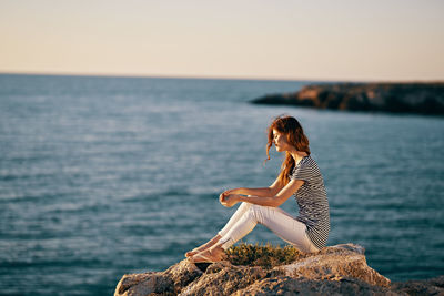 Woman sitting on rock by sea against sky