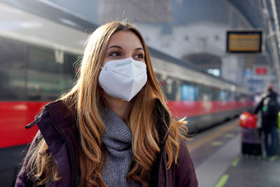 Girl wearing kn95 ffp2 medical face mask with moving train on background on train station