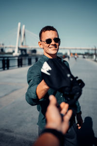 Portrait of man holding sunglasses while standing against sky
