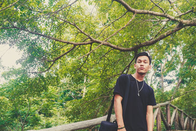 Young man looking away while standing by tree in forest