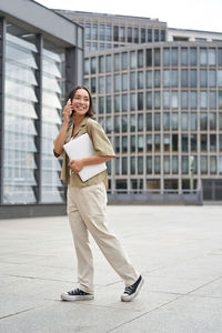 Full length of young woman standing against building