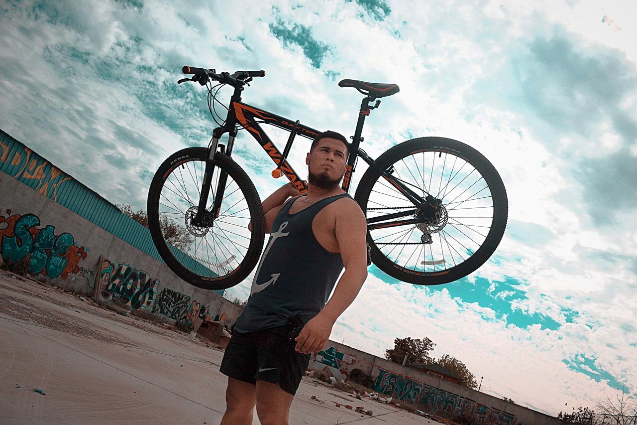 MAN WITH BICYCLE STANDING AGAINST THE SKY