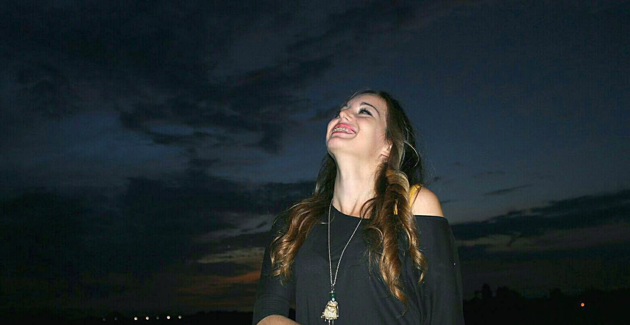 WOMAN LOOKING UP WHILE STANDING IN ILLUMINATED AT NIGHT