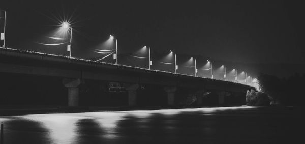 Illuminated bridge over river against sky at night