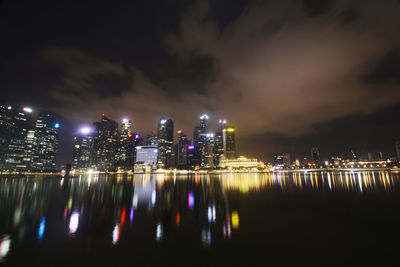 Illuminated buildings by river against sky at night