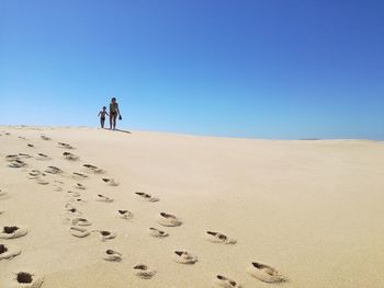 People walking on sand dune in desert against clear blue sky