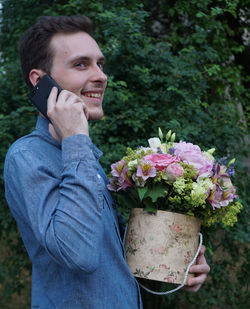 Smiling man using phone holding bouquet