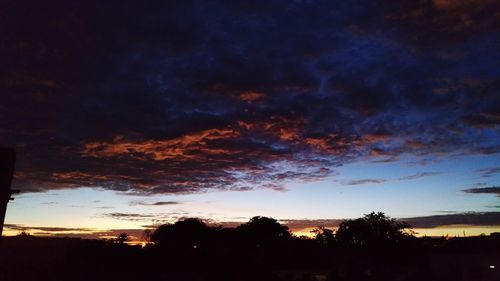 Silhouette trees against dramatic sky at sunset