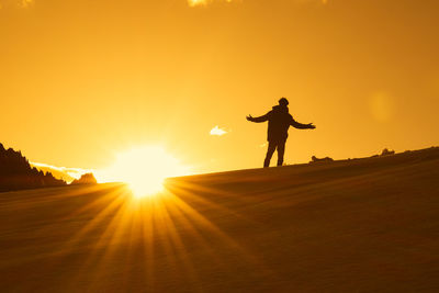 Rear view of woman walking on field against sky during sunset