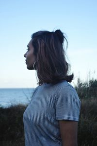 Side view of young woman standing on field against sky at dusk