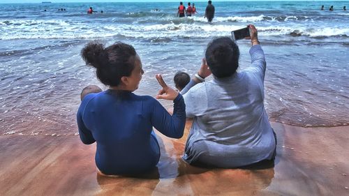 Rear view of friends photographing at beach