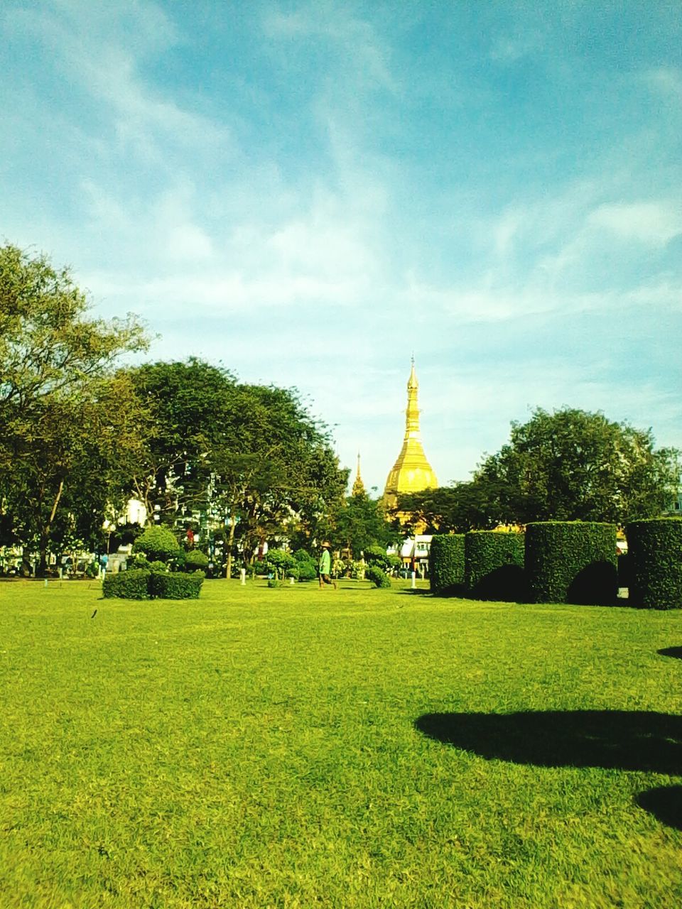 tree, sky, religion, architecture, built structure, place of worship, spirituality, grass, green color, famous place, building exterior, travel destinations, lawn, cloud - sky, tourism, travel, church, park - man made space