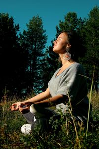 Side view of woman meditating on grass against trees