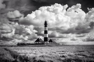 Lighthouse on field against cloudy sky