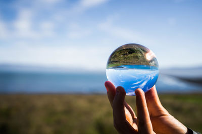 Close-up of hand holding crystal ball against sea