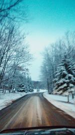 Road amidst trees against clear sky during winter