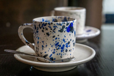 White coffee cup with blue spots on a saucer with a spoon on a wooden table close up