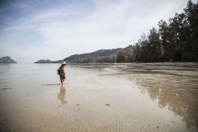 Woman collecting oysters on beach against sky