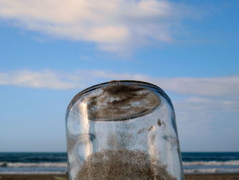 Close-up of glass on beach against sky