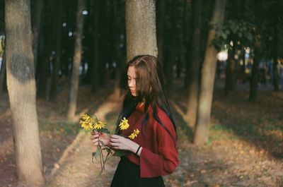 Young woman standing by tree trunk in forest