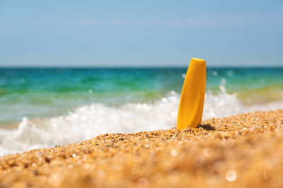 Yellow bottle of sunscreen on a golden beach next to the waves of the sea and foam against the
