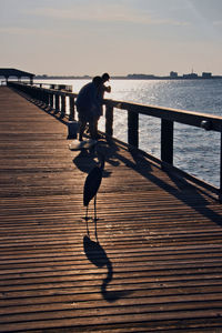 Man on pier by sea against sky during sunset