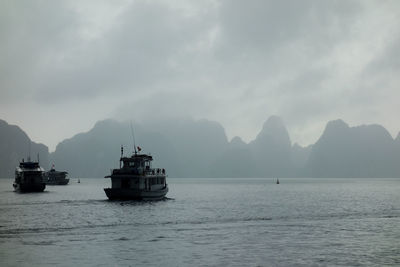 Ships sailing in sea against cloudy sky