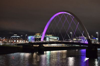 Illuminated bridge over river against sky in city at night