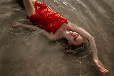 Girl in a red dress lies in sea water high angle