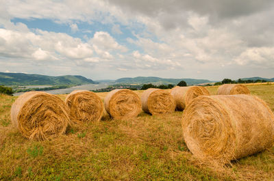 Hay bales on agricultural field against cloudy sky