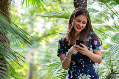 Young woman using mobile phone against trees