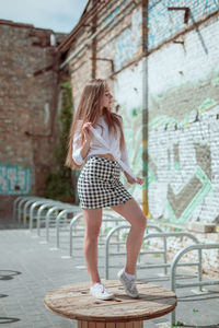 Full length of woman standing on wooden spool against building