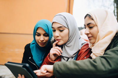 Young female muslim friends sharing digital tablet in city