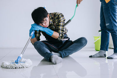 Low section of woman standing by tired man leaning on mop against wall