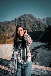 Portrait of young woman standing against mountain