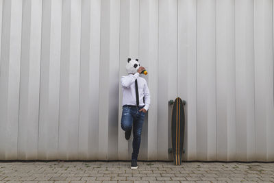 Businessman with a longboard skateboard and panda bear mask having coffee